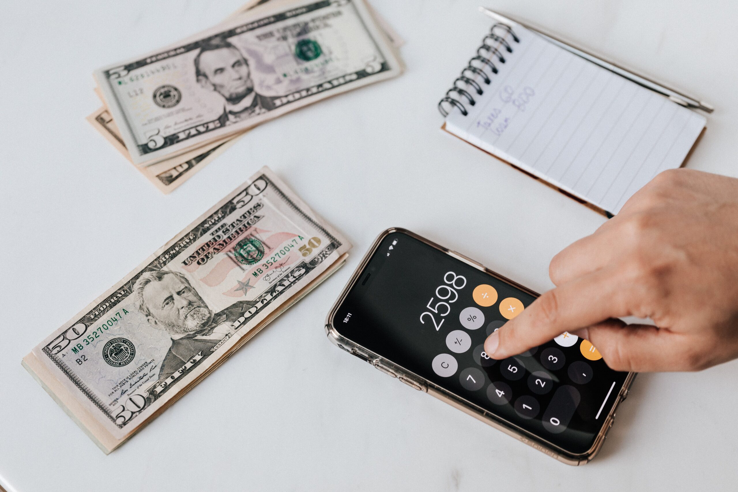 Someone using calculator on smartphone near stack of money