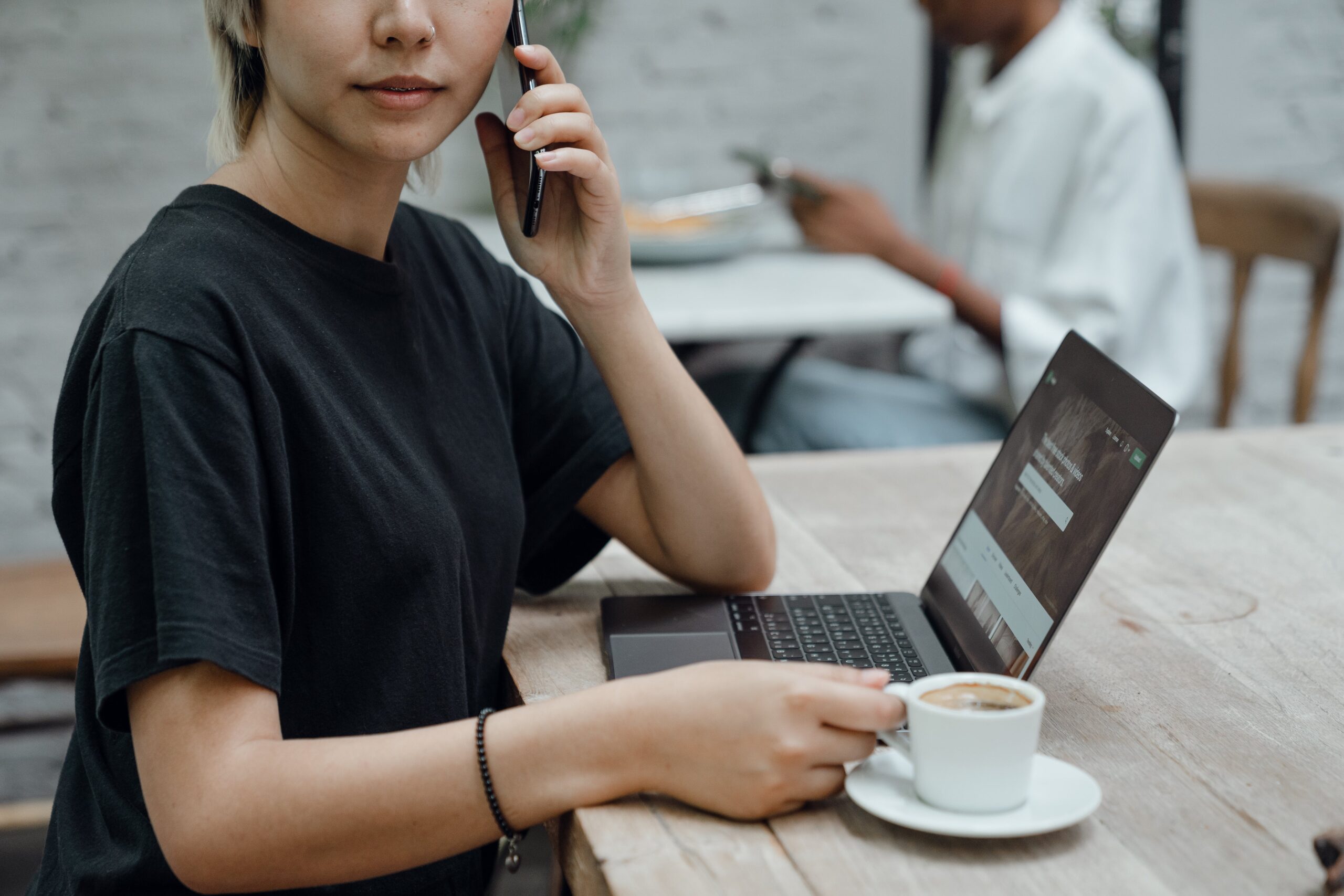 Woman talking on cell phone with coffee and laptop